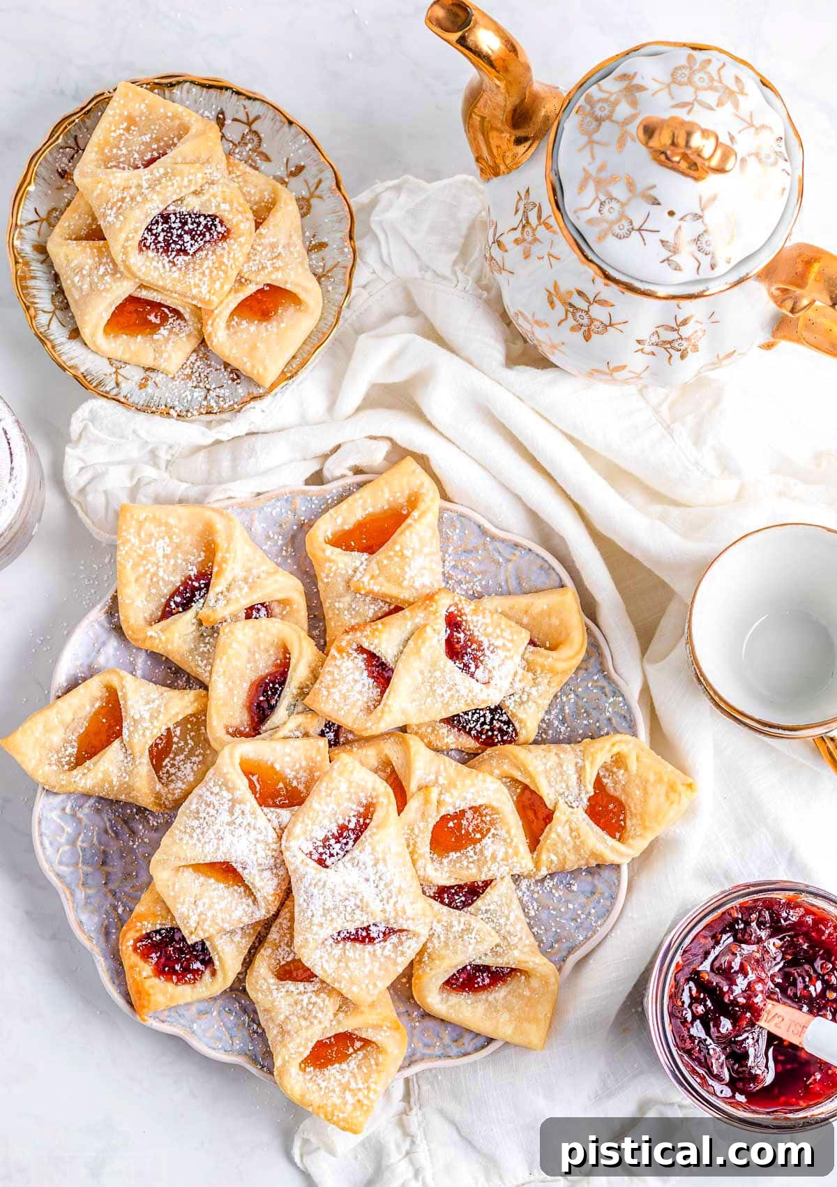 Kolaczki Beloved Polish Pastries 3 A charming flat lay view of a plate adorned with freshly baked Kolacky cookies, artfully dusted with powdered sugar. A small, inviting jar of jam sits gracefully in the lower right corner, suggesting the delightful filling within.