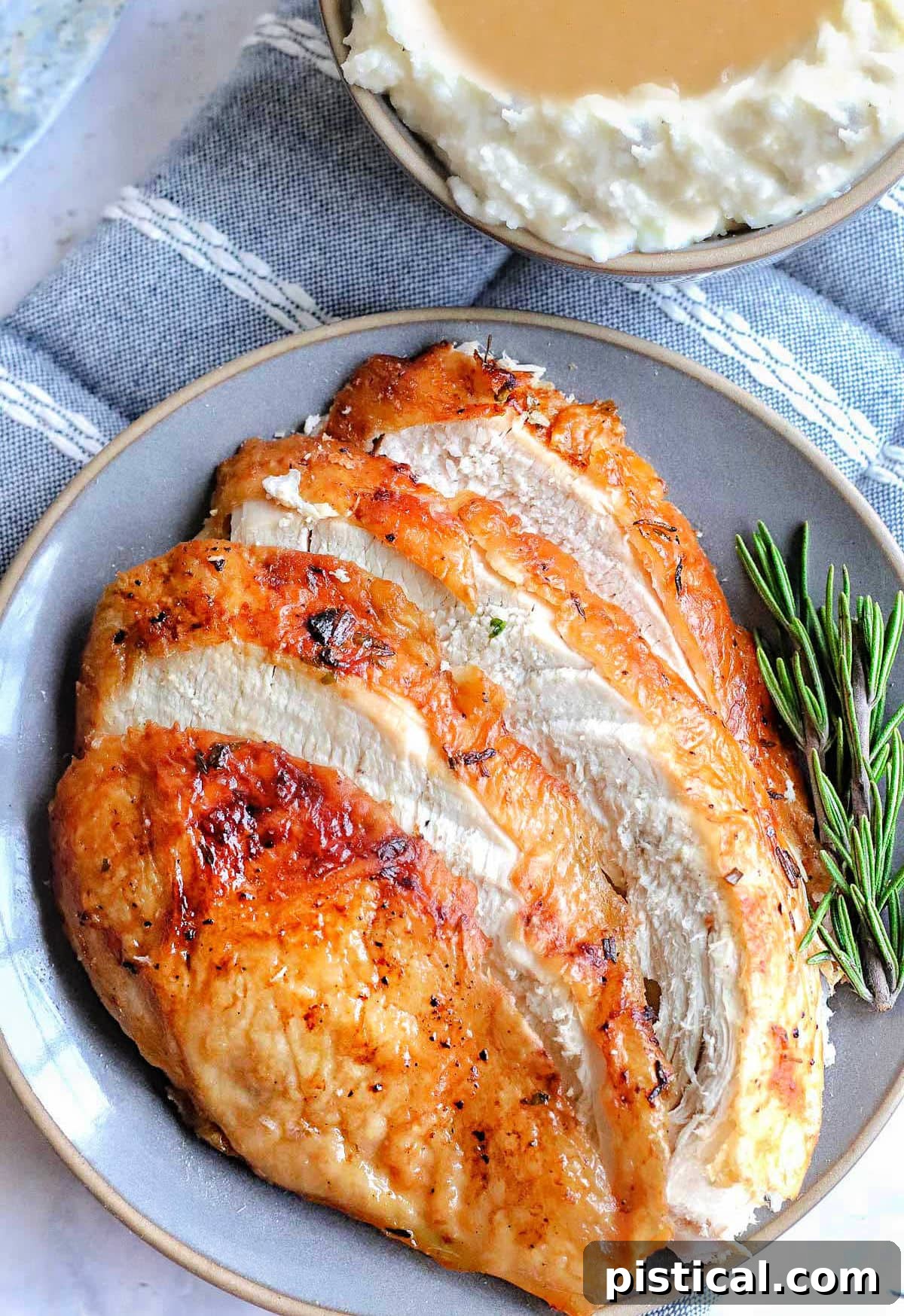 Slices of air fryer turkey breast fanned out on a gray plate next to a small bowl of mashed potatoes and gravy.