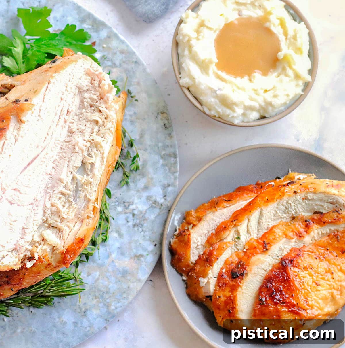 top down shot of carved turkey breast and slices of turkey breast on a plate. a small bowl of mashed potatoes is off to the side.