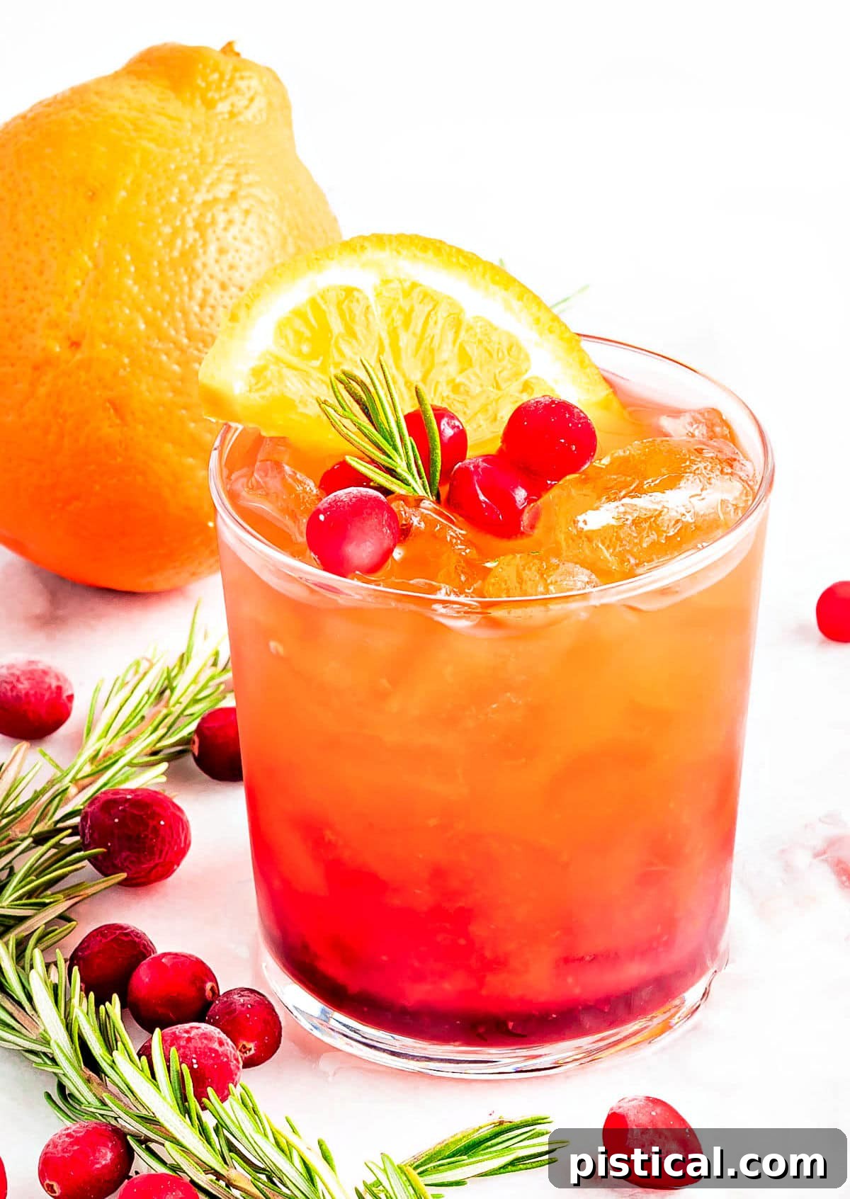 A stunning crystal glass filled with a vibrant red Christmas Punch, beautifully garnished with fresh rosemary, glistening cranberries, and a bright orange slice, set against a festive backdrop.