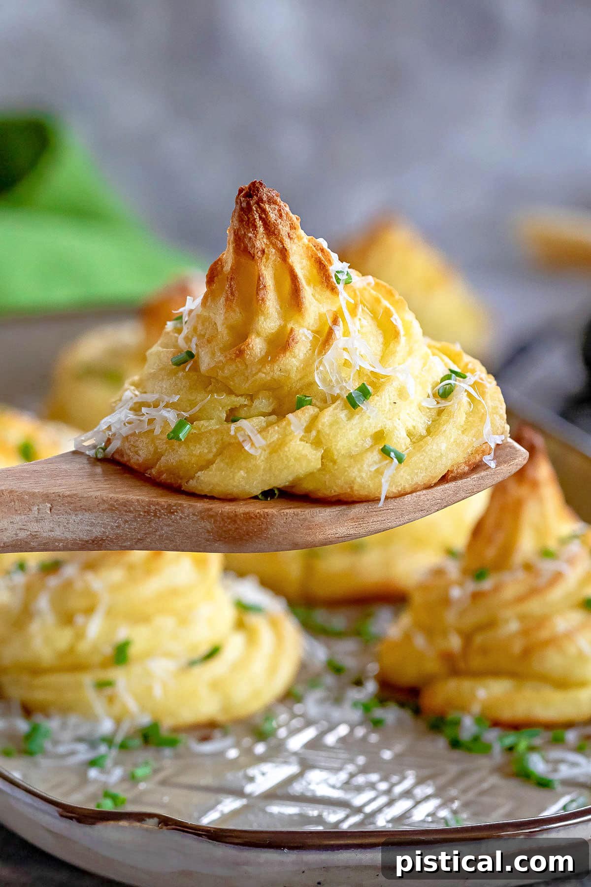 Golden Potato Swirls 8 single Duchess potato held up above a tray with a wooden server. granished with chives and Parmesan.