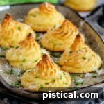 large brown tray with six duchess potatoes garnished with Parmesan cheese and snipped chives.