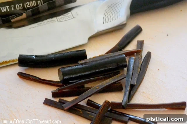 Close-up showing black tube licorice being cut into thin strips to form spider legs for Oreo cookies