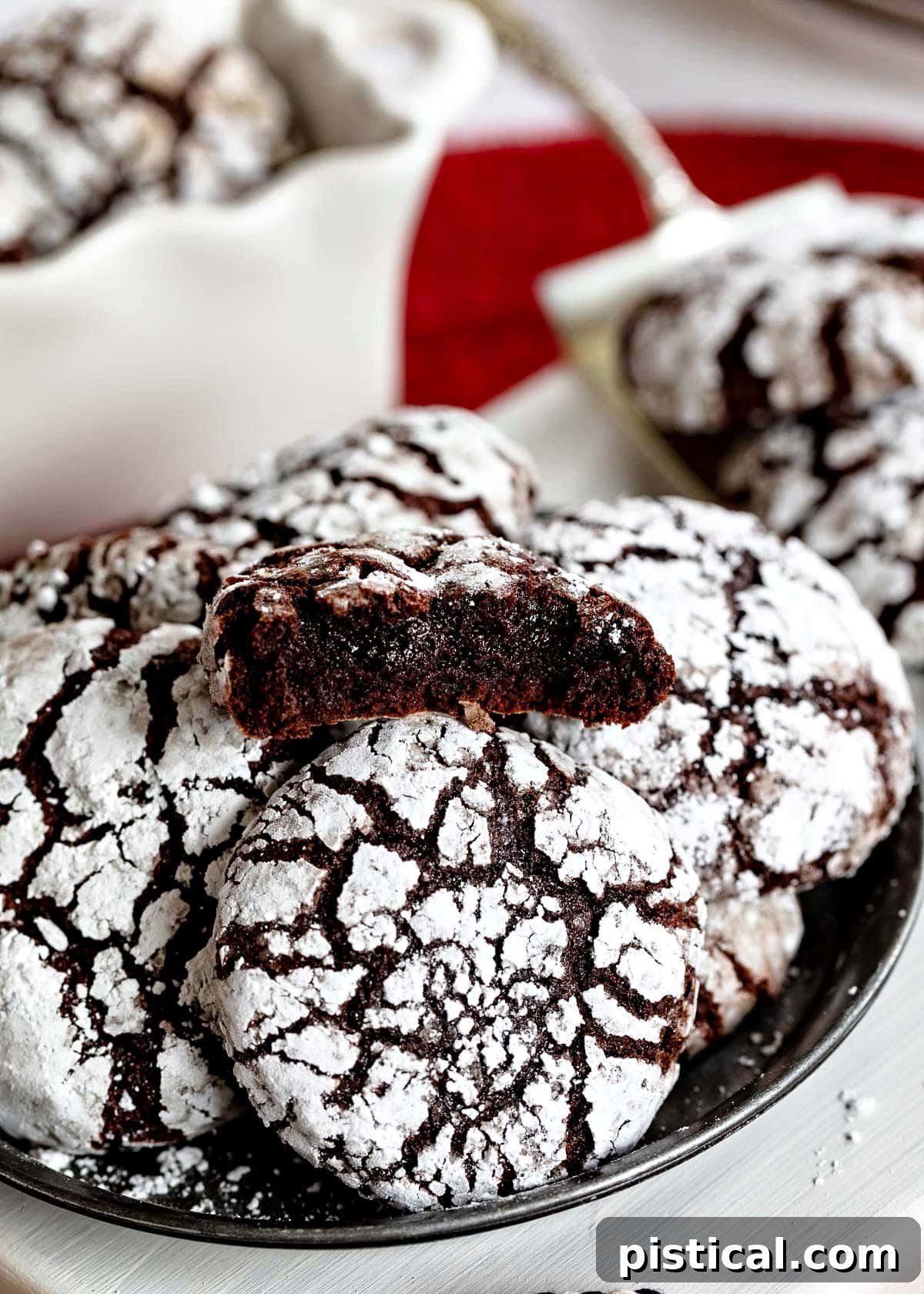 Plate of crinkle cookies with the top cookie broken in half showing the moist, fudgy chocolate interior, emphasizing their brownie-like texture.