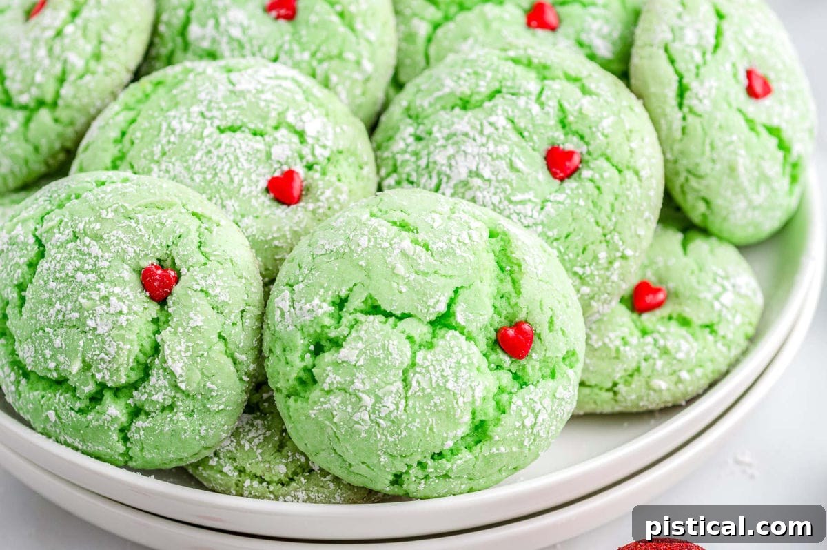 Two white plates stacked high with freshly baked green Grinch Cookies, each adorned with a vibrant red heart sprinkle.