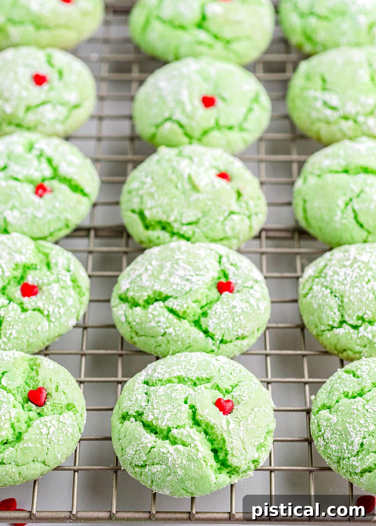 Grinch Cookies cooling on a wire rack, each perfectly green with a red heart sprinkle pressed into the top.