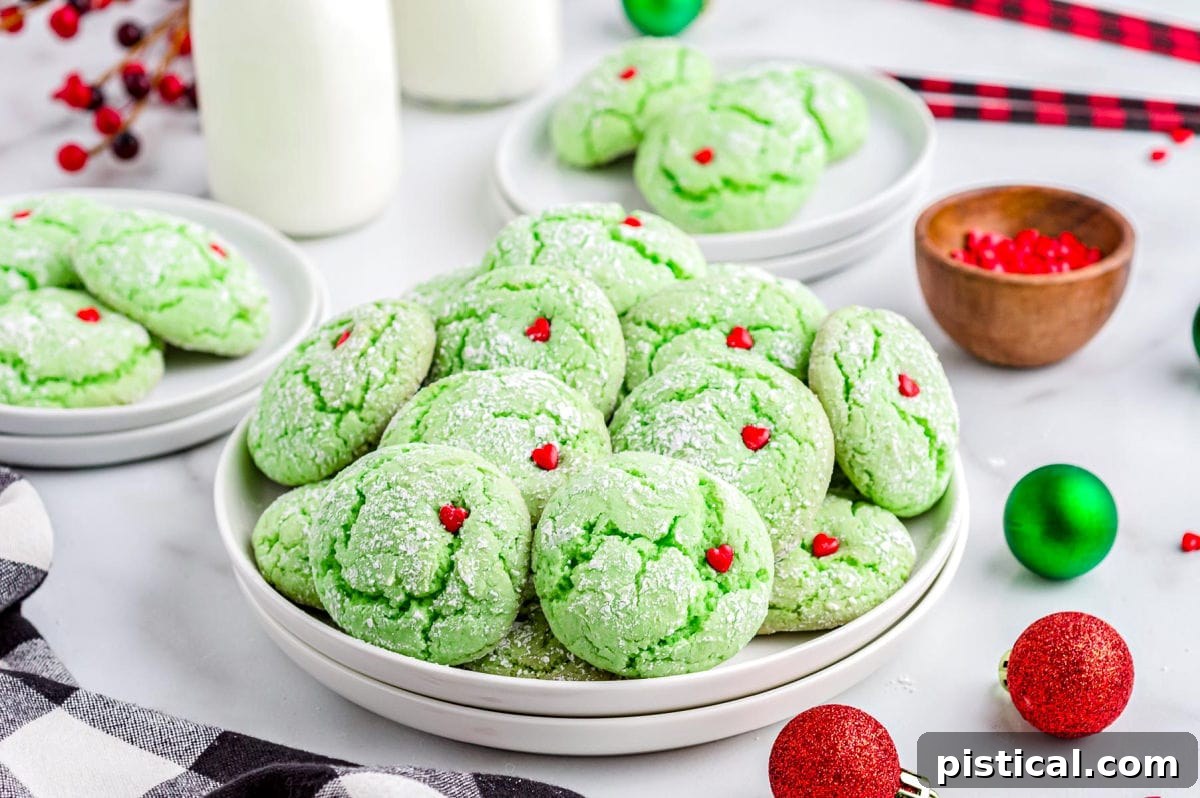 A festive display of green Grinch Cookies with red heart sprinkles, arranged on a white plate with milk bottles and Christmas decorations in the background, ready for the holidays.