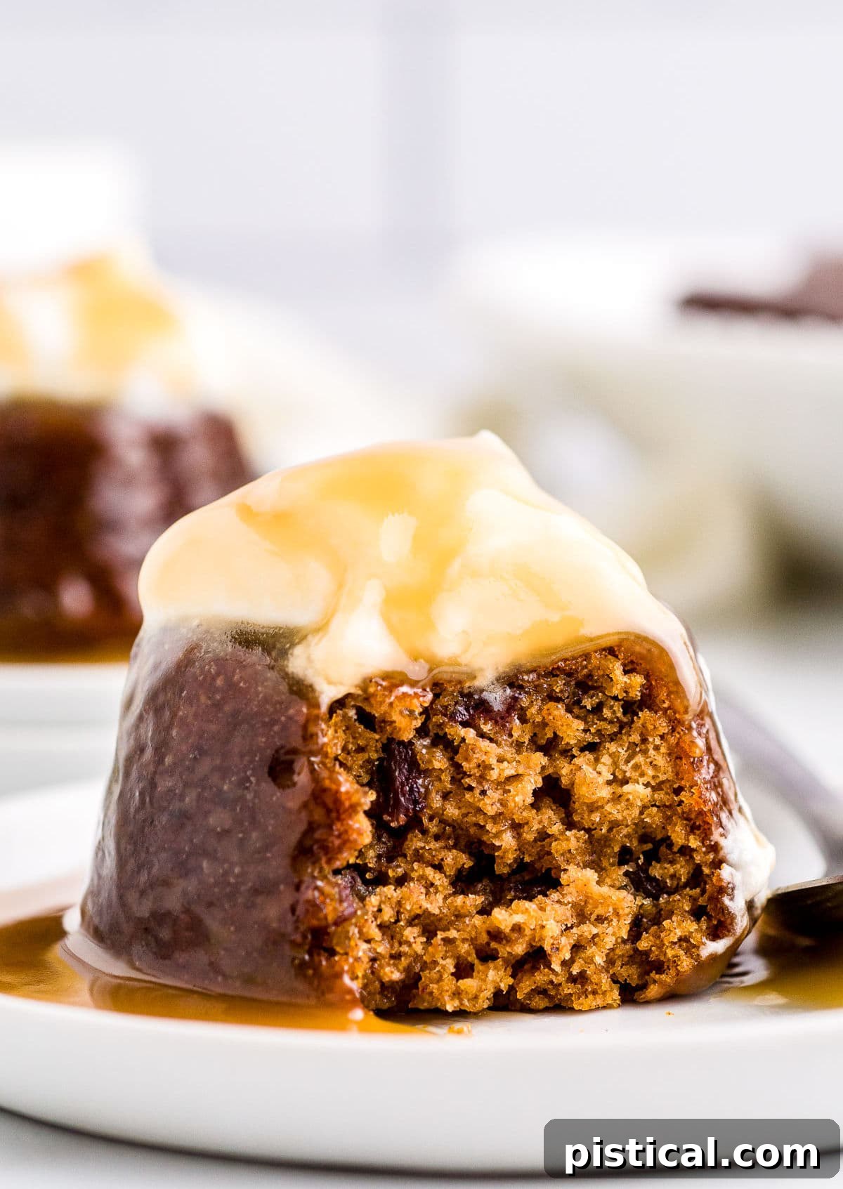 A single sticky toffee pudding on a white dessert plate, elegantly topped with fluffy whipped cream and a generous drizzle of golden toffee sauce.