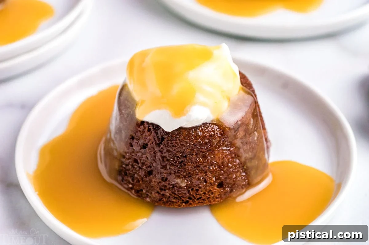 An inviting angled view of one sticky toffee pudding, crowned with whipped cream and glistening with more toffee sauce, presented on a simple white dessert plate.