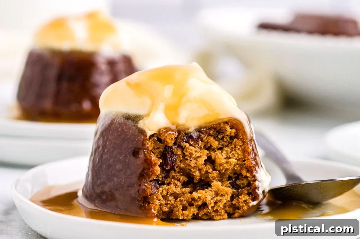A sticky toffee pudding on a white dessert plate, beautifully garnished with whipped cream and an abundant pour of golden toffee sauce.