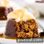 sticky toffee pudding on white dessert plate topped with whipped cream and toffee sauce.