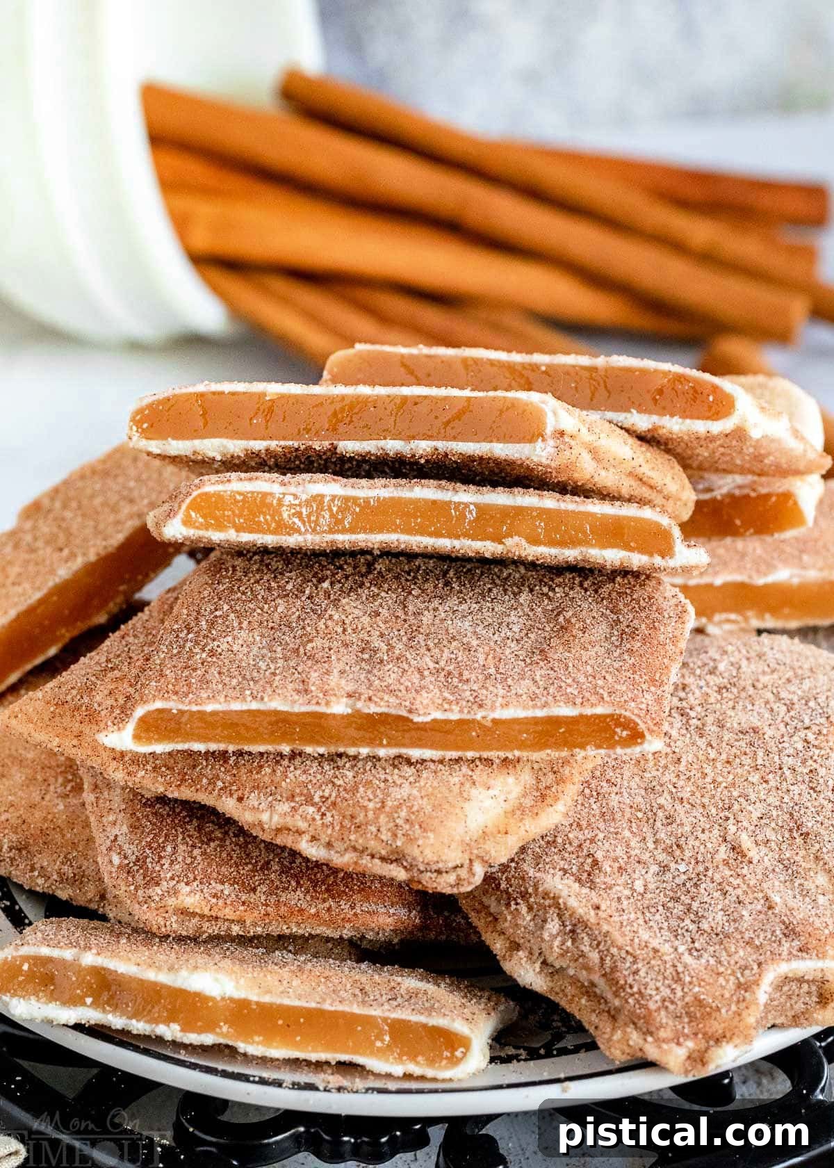 A charming pile of Churro Toffee squares arranged on a black and white plate, with decorative cinnamon sticks in the background.