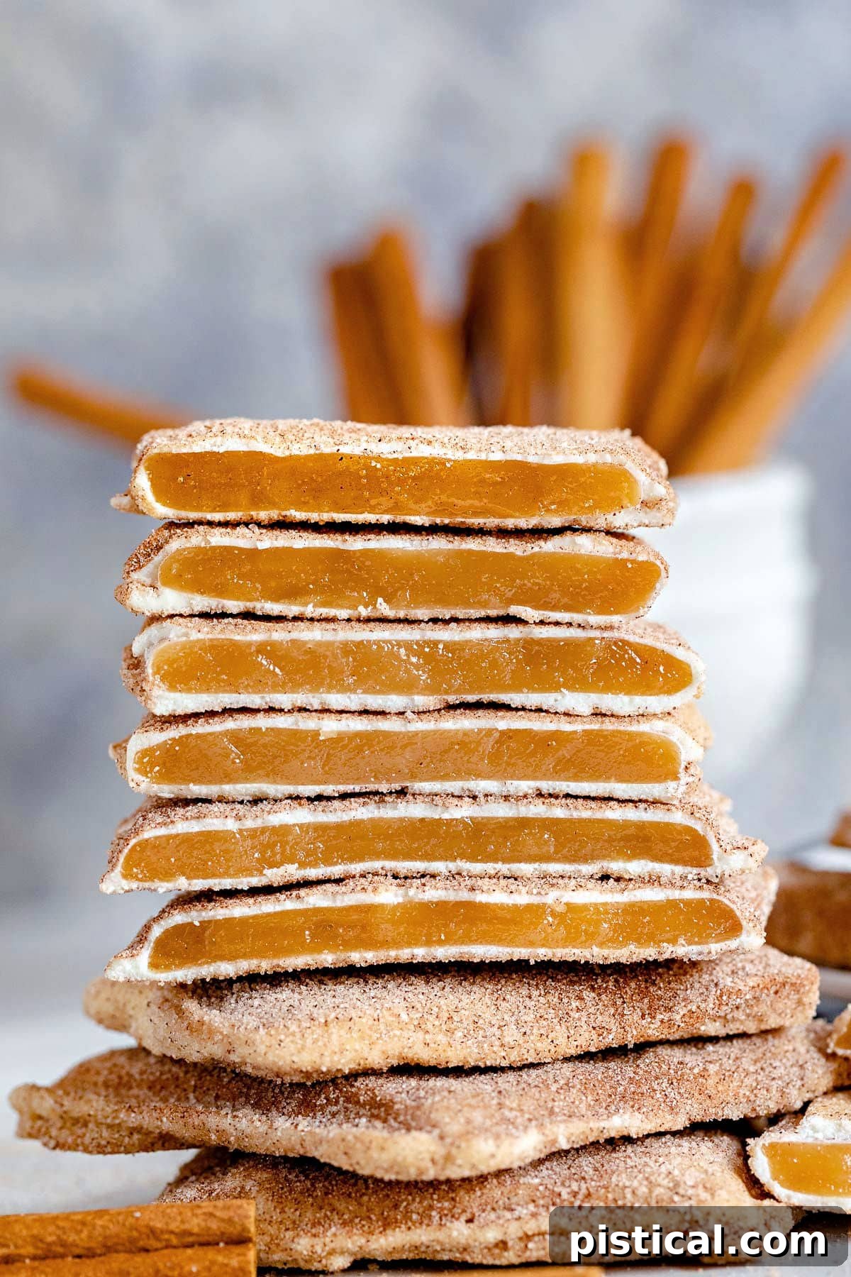 Beautifully arranged Churro Toffee squares, some broken to showcase the layers, with cinnamon sticks in the background, suggesting a festive ambiance.