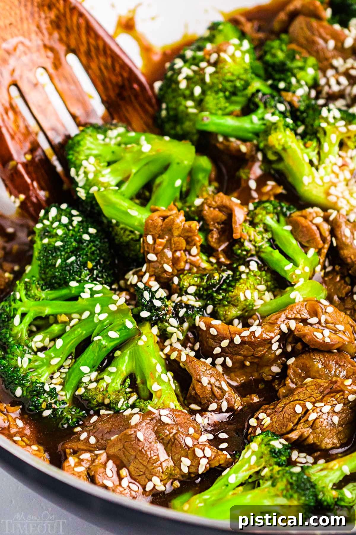 Savory Beef and Broccoli Stir-fry 2 beef and broccoli stir fry topped with sesame seeds in white skillet with wood serving spoon.