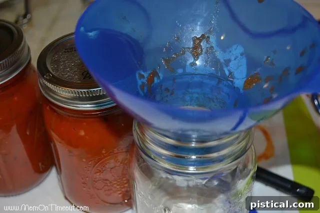 Hot homemade pasta sauce being carefully poured into glass canning jars with a funnel.