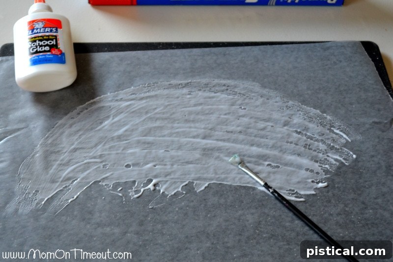Child applying white school glue onto a piece of waxed paper using a paintbrush.