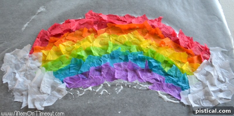 Stained glass tissue paper rainbow craft with white tissue paper clouds added to the ends.