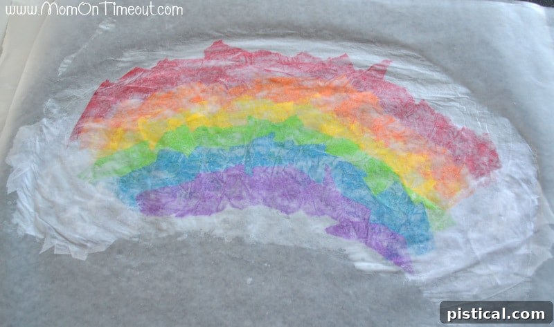 Covering the tissue paper rainbow with a second layer of glue-covered waxed paper to seal it.