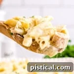 wooden spoonful of chicken alfredo bake held above baking dish.