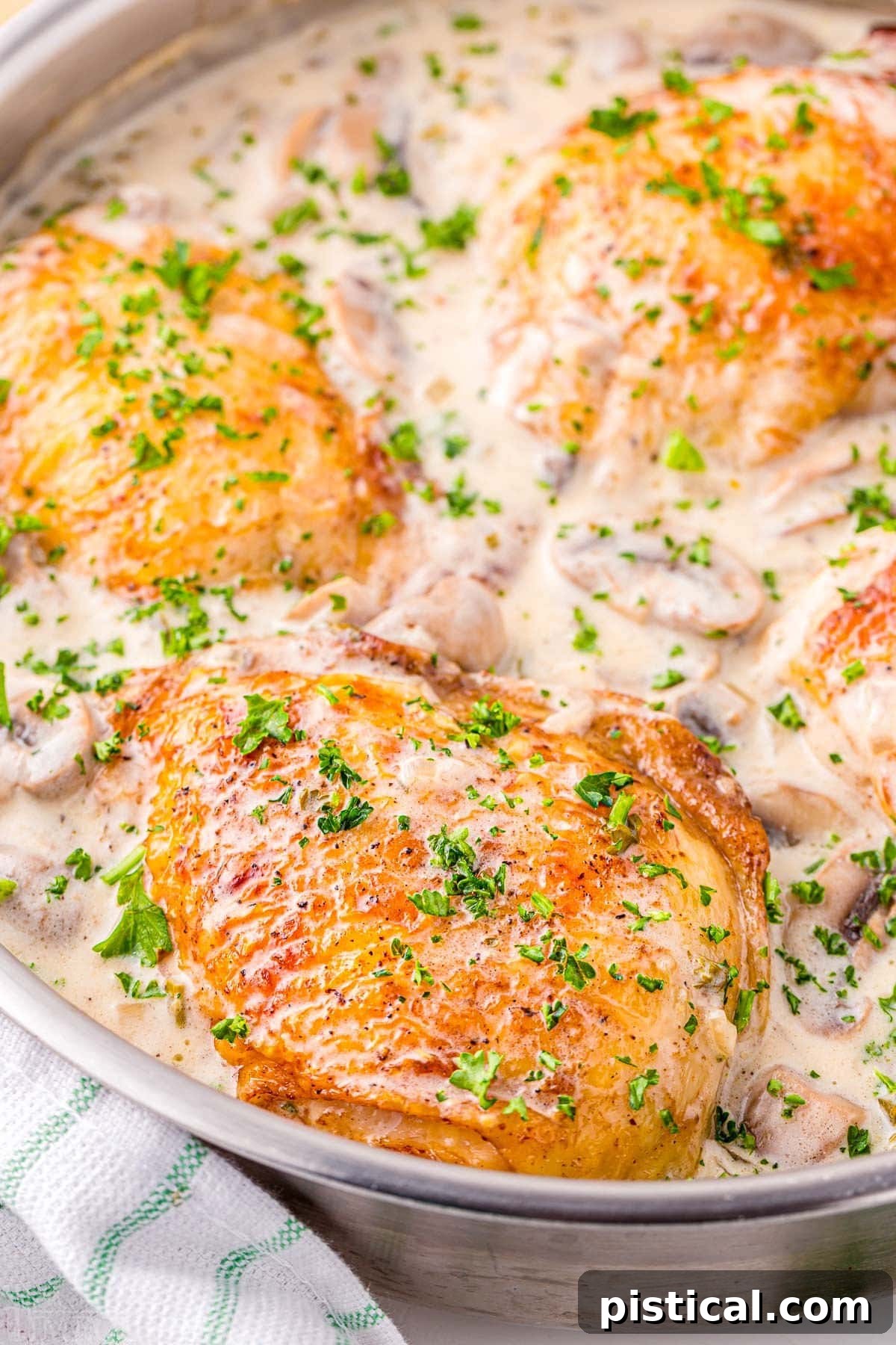 Golden-brown chicken thighs simmering in a creamy white wine mushroom sauce, garnished with fresh parsley in a cast iron skillet.