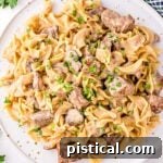 Top down view of a white plate filled with Instant Pot Beef Stroganoff, ready to be enjoyed. Parsley and mushrooms are in the background.