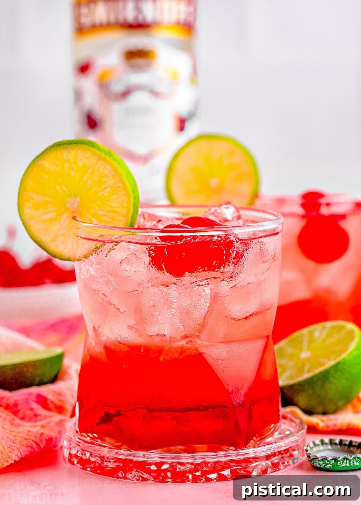 two dirty shirley temple cocktails garnished with lime and maraschino cherries with the bottle of vodka in the background.