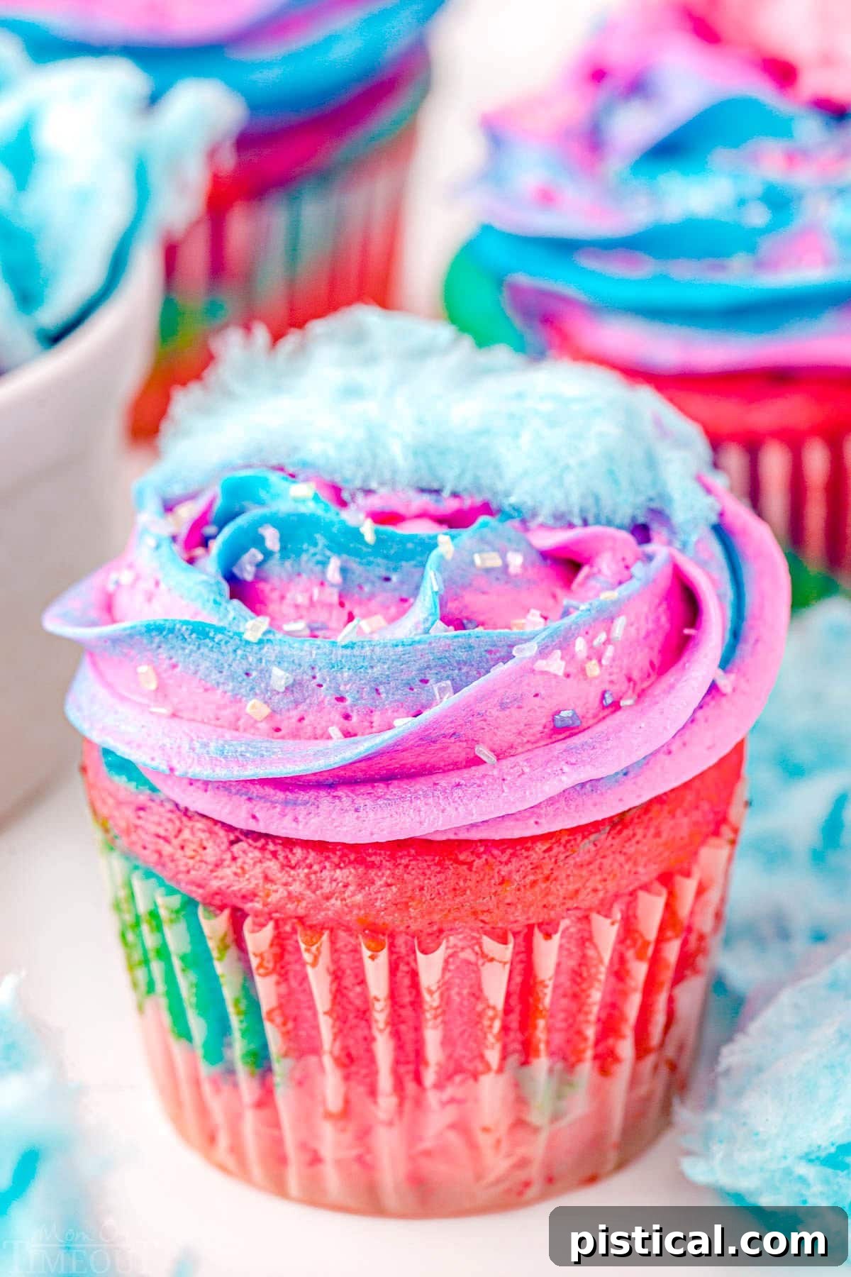 Close-up view of a swirled cupcake featuring vibrant blue and pink frosting, topped with a small, fluffy piece of cotton candy.