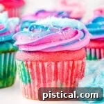 cotton candy cupcakes decorated with pink and blue frosting and topped with cotton candy ready to be enjoyed. Bits of cotton candy are scattered around the cupcakes as well.
