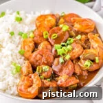 Foolproof Gumbo 7 gumbo recipe served on a white plate next to a scoop of white rice and topped with sliced scallions.