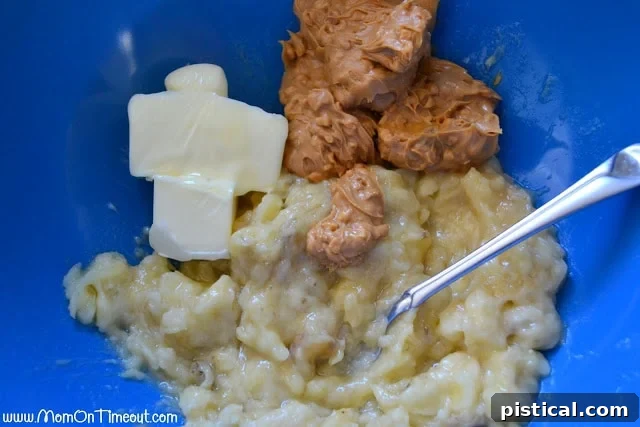 A blue mixing bowl filled with a creamy mixture of mashed bananas, melted butter, and chunky peanut butter, awaiting further ingredients.