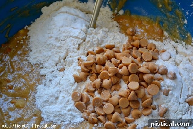 A mixing bowl showing the peanut butter banana bread batter, with both dry flour mixture and Reese's Peanut Butter chips freshly added, awaiting a final gentle stir.