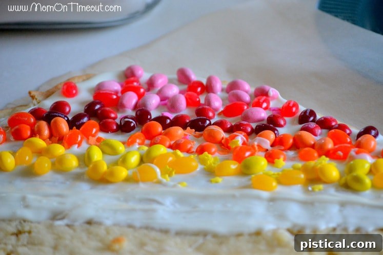 Step-by-step: Adding colorful candies to create the rainbow design on the sugar cookie bark. Adding colorful candies in rows onto the vanilla candy coating spread over a sugar cookie base