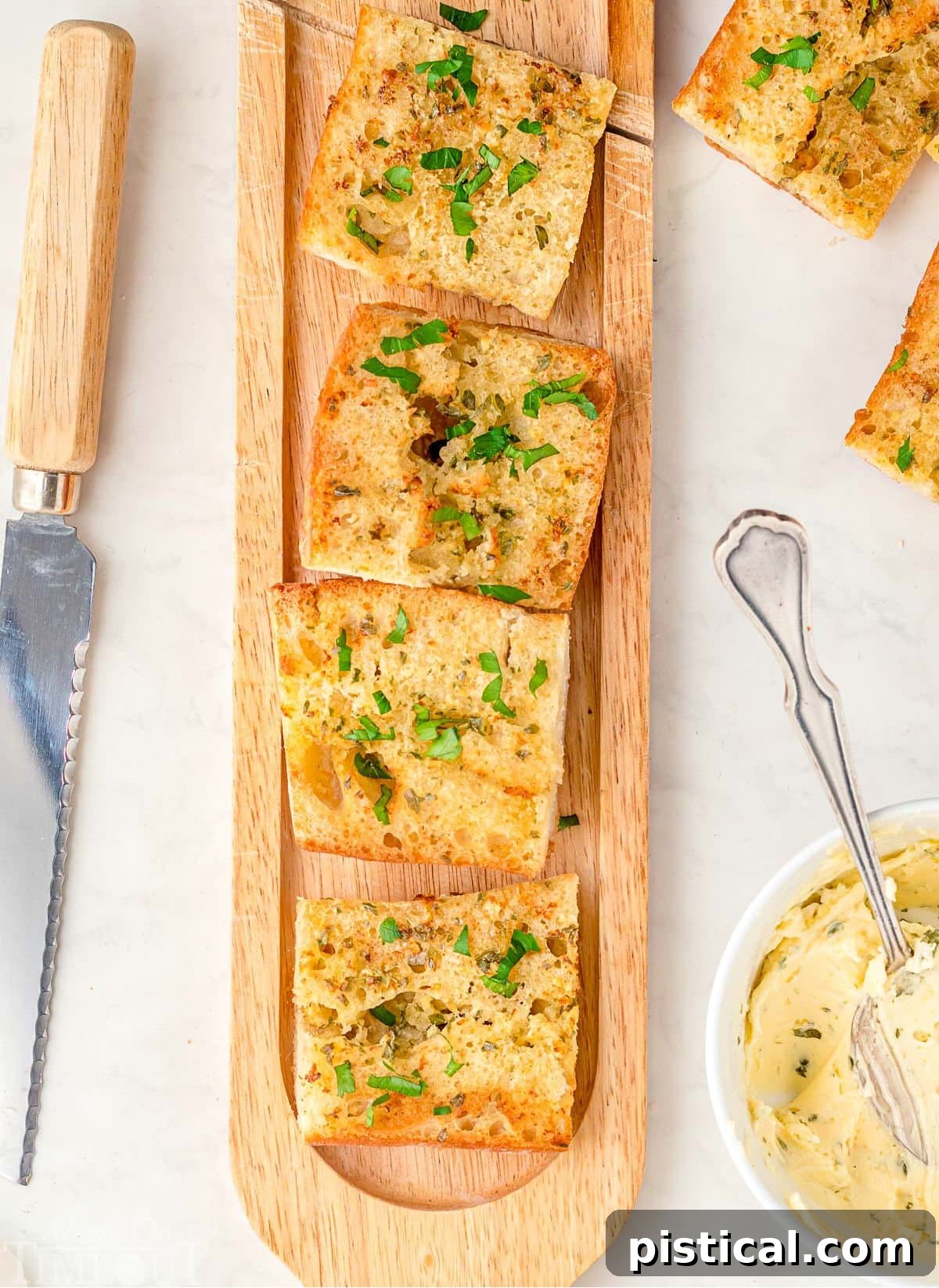 A rustic wood board displaying freshly cut pieces of golden Air Fryer Garlic Bread. A small bowl of homemade garlic butter sits alongside, with extra bread pieces and a knife nearby.
