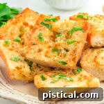A shot of golden Air Fryer Garlic Bread, perfectly sliced and garnished with fresh parsley, ready to serve from a white plate.