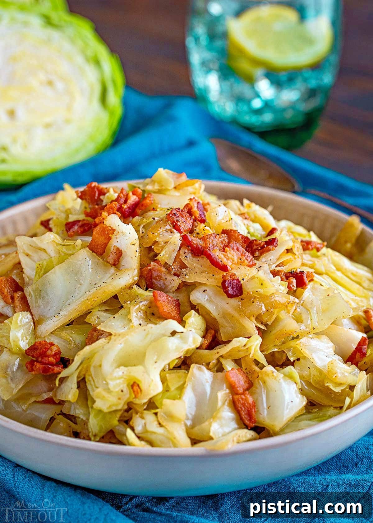shallow bowl filled with fried cabbage made with bacon, onion and garlic. The bowl is sitting on a bright teal napkin and half a head of cabbage is in the background.