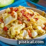 shallow bowl filled with fried cabbage made with bacon, onion and garlic. The bowl is sitting on a bright teal napkin and half a head of cabbage is in the background.