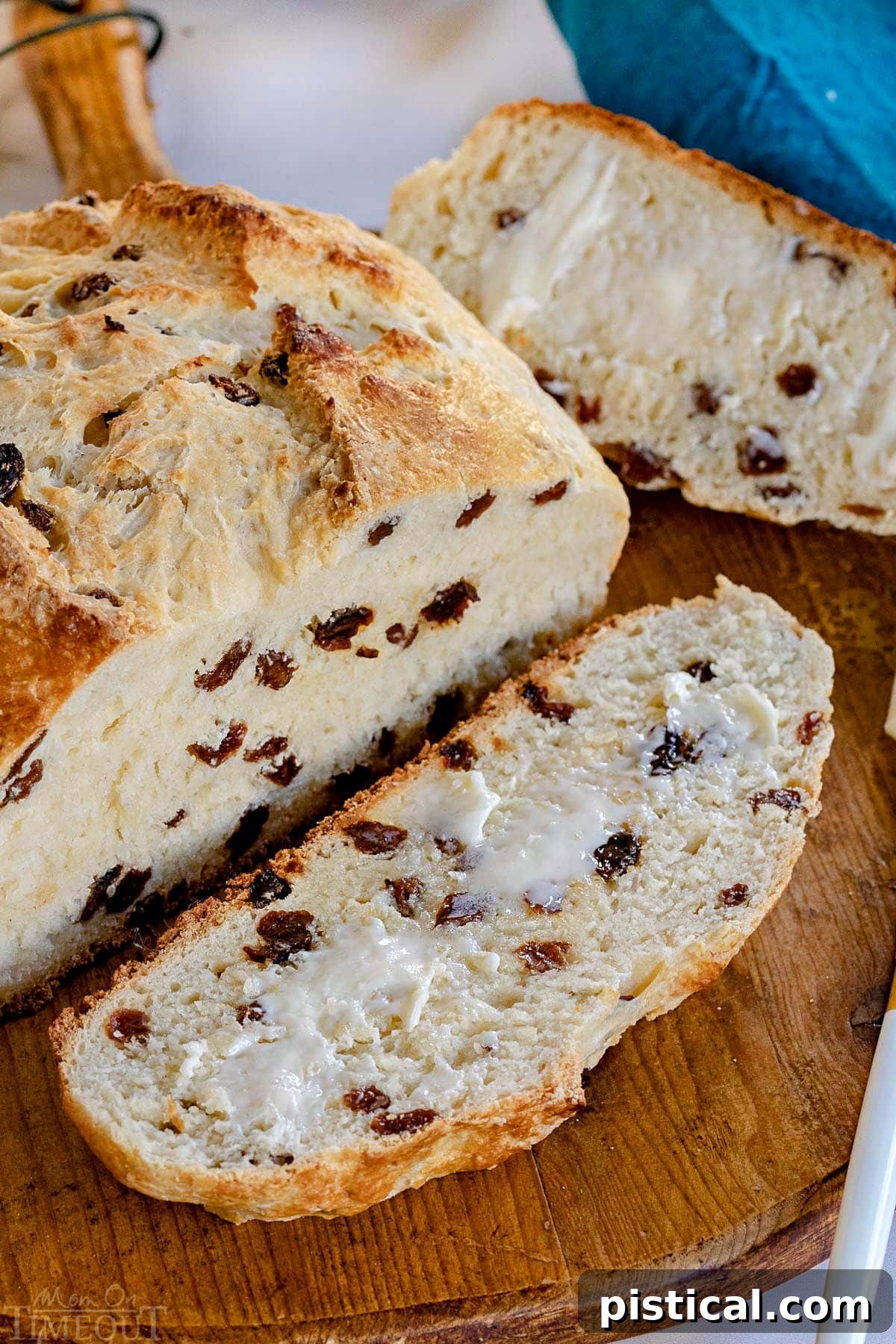 A beautifully baked loaf of Irish Soda Bread, with one slice cut off and buttered, resting on a rustic round wooden board. The bread is golden brown and looks incredibly inviting.