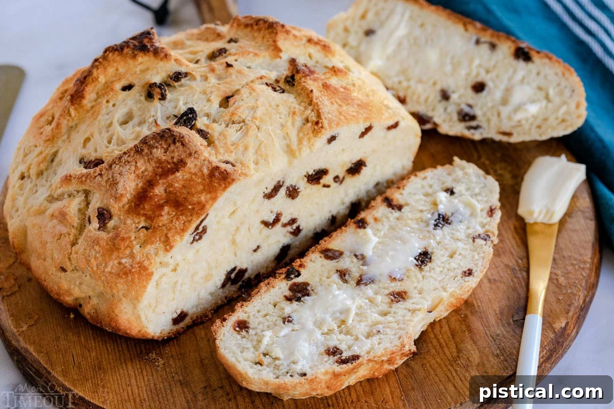 A beautiful top-down view of an Irish Soda Bread loaf with one slice buttered and placed artfully on a round wooden board, inviting you to take a bite.