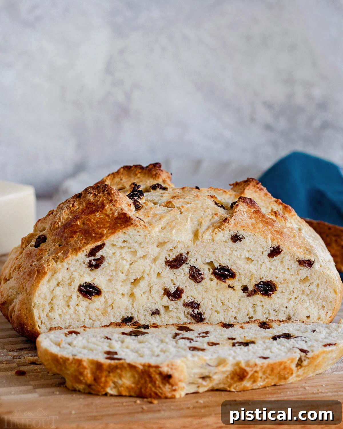 A rustic loaf of Irish Soda Bread with a slice cut off, beautifully presented on a wooden cutting board with a soft blue napkin in the background.