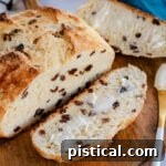 A top-down view of a freshly baked Irish Soda Bread loaf, with one slice cut and buttered, presented on a rustic round wooden board.