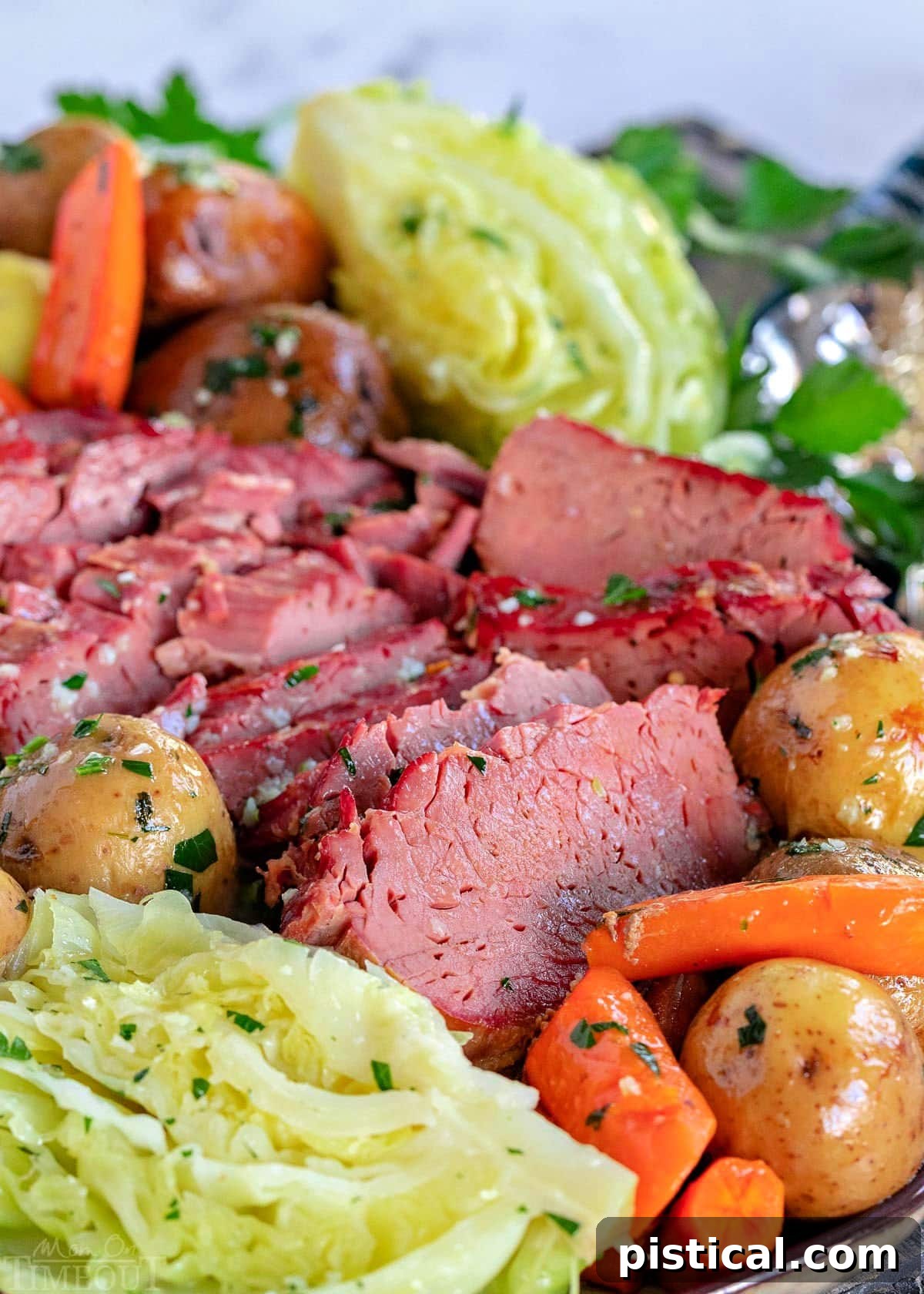 close up look at slices of slow cooker corned beef and cabbage wedges plus potatoes and carrots on a serving platter brushed with garlic herb butter.