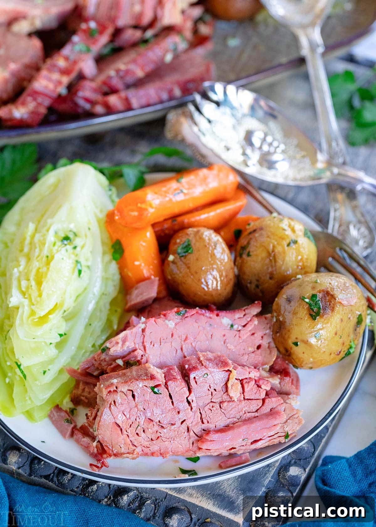 plate with a few slices of corned beef and cabbage, potatoes and carrots sitting on a gray wood board with serving plate in background.