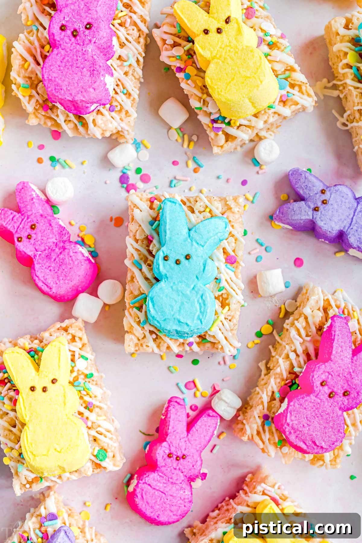 Gooey Peeps Krispie Delights 2 rice krispie treats decorated with white candy melts and sprinkles and topped with different colored Peeps. This is a top down view of the treats laid out on parchment paper.