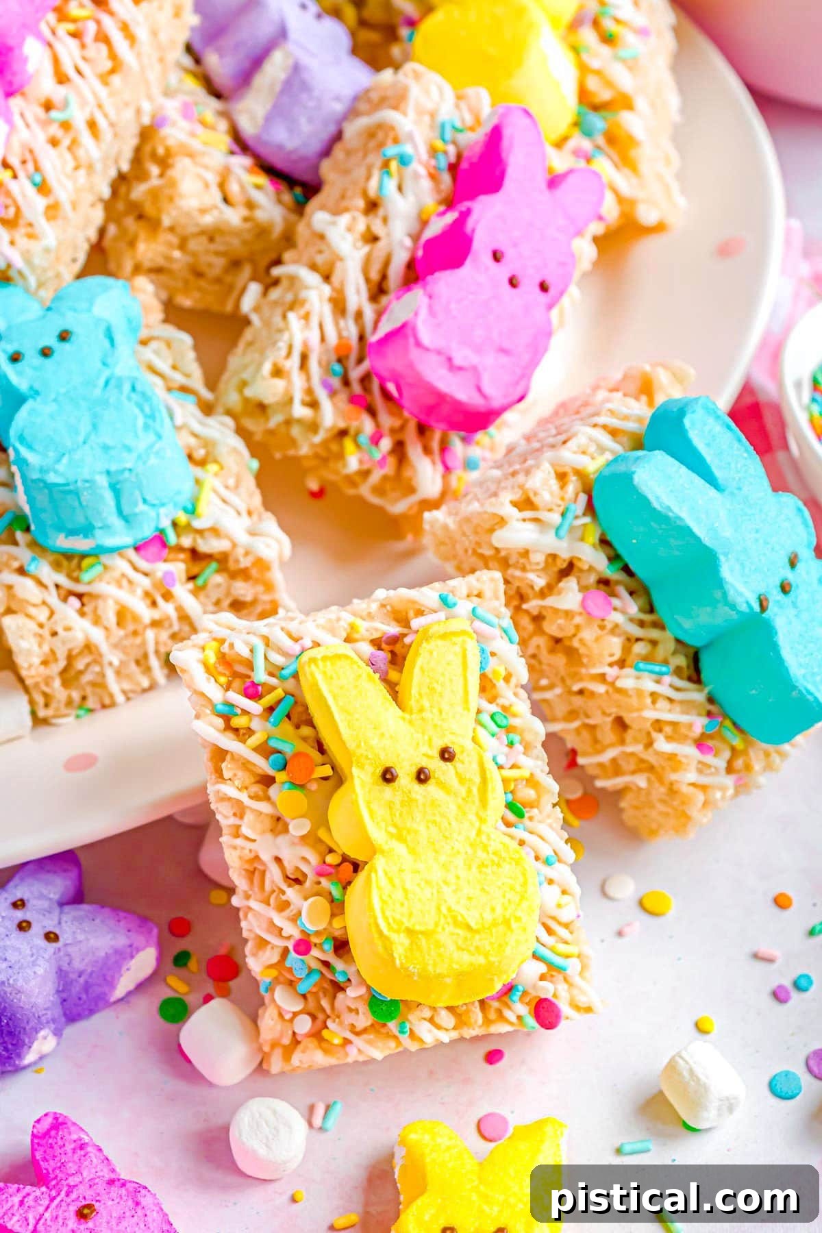 Gooey Peeps Krispie Delights 6 a number or rice krispie treats decorated with sprinkles and topped with an Easter peep sitting on a white plate and a few around the plate.