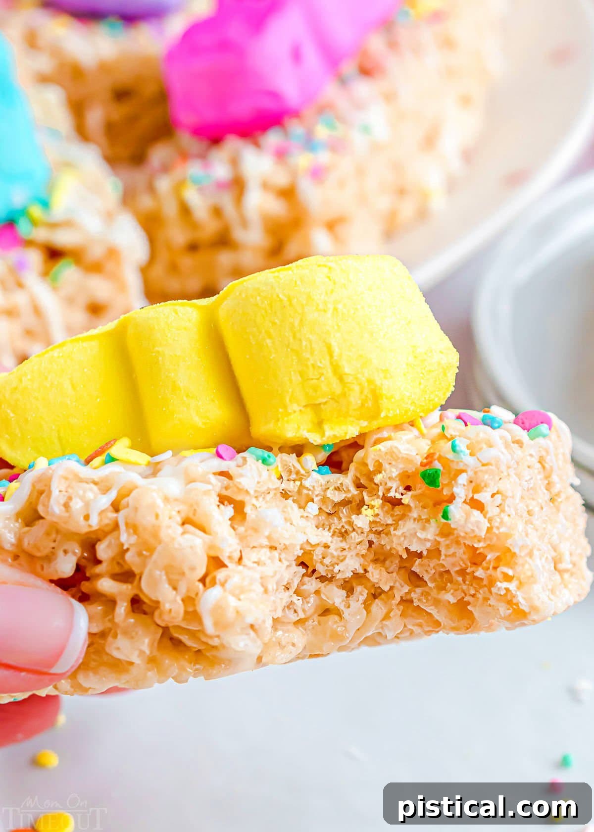 Gooey Peeps Krispie Delights 7 a treat held up with a bite taken out of it. a yellow peep is on top of the rice krispie treat.