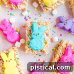 Gooey Peeps Krispie Delights 8 rice krispie treats decorated with white candy melts and sprinkles and topped with different colored Peeps. This is a top down view of the treats laid out on parchment paper.