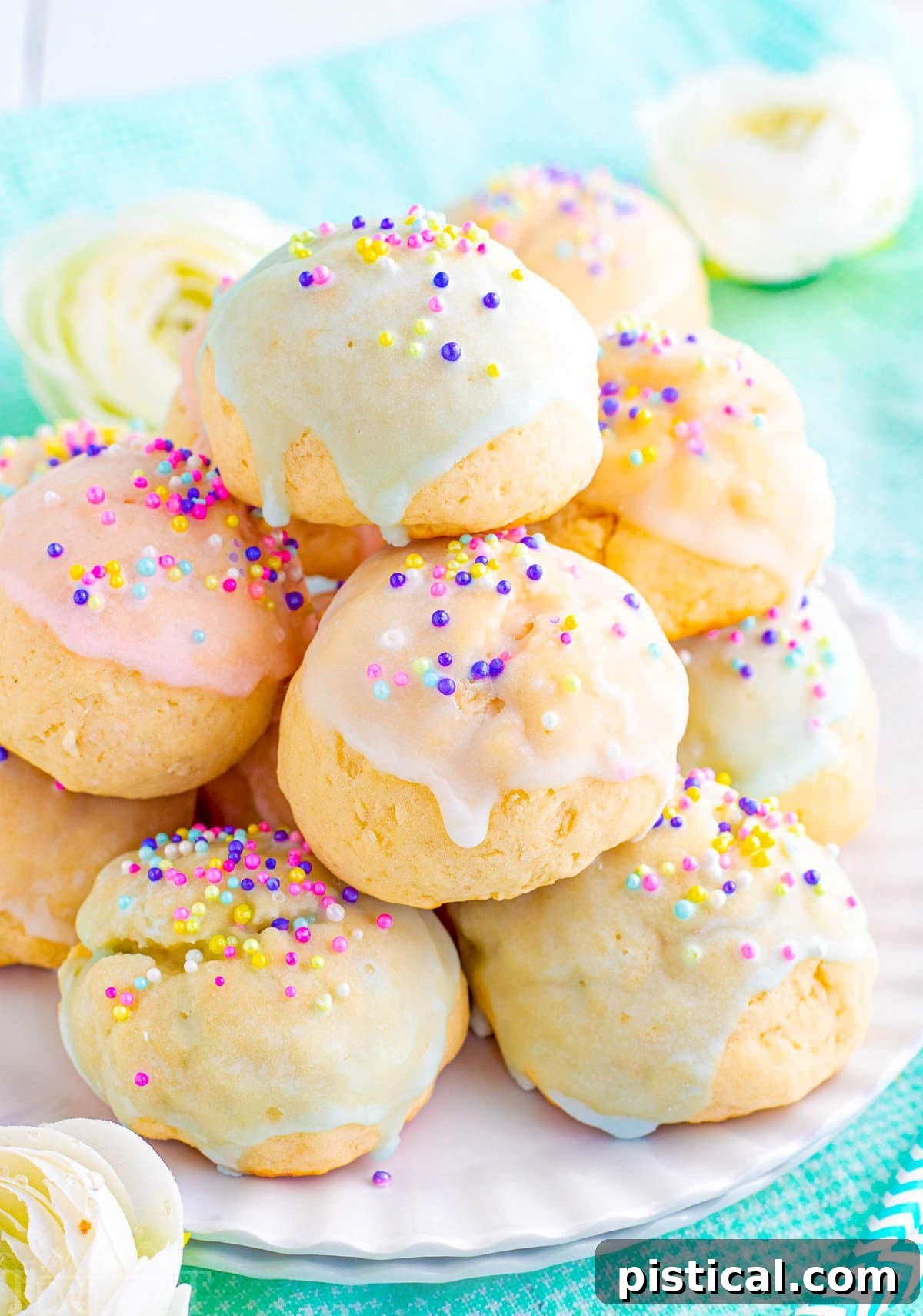 Colorful Italian cookies piled high on a white scalloped plate. Cookies are topped with sprinkles and pastel glaze in varying colors.