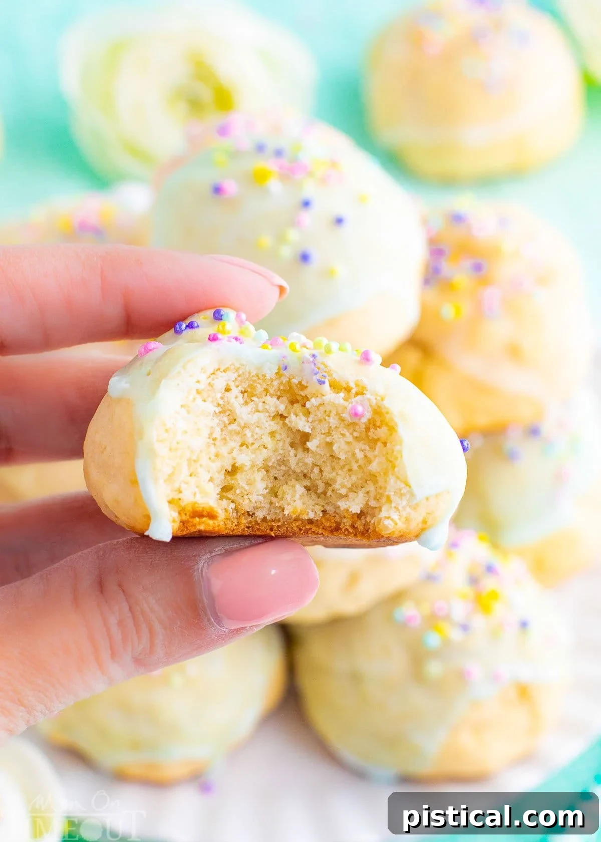 An Italian Cookie held up with a bite out of the cookie. More cookies on a plate can be seen in the background.