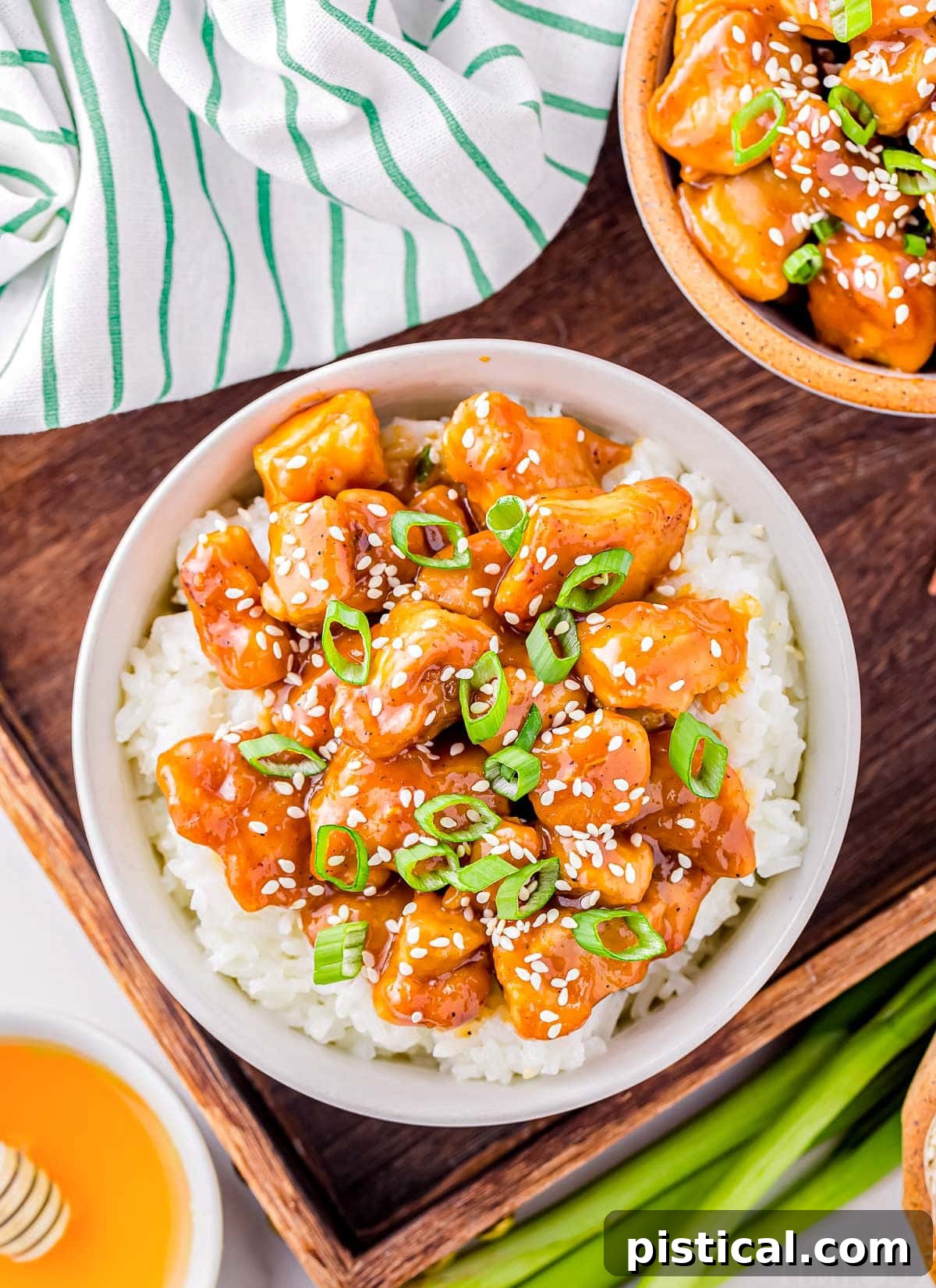 Sticky Honey Garlic Chicken 3 top down look at white bowl filled with steamed white rice and topped with honey garlic chicken. bowl is garnished with sesame seeds and sliced green onions.