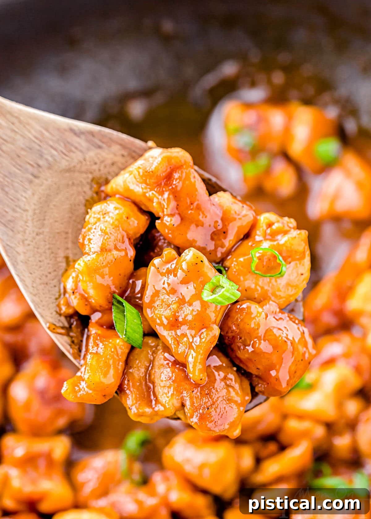 Sticky Honey Garlic Chicken 4 wooden spoon held above skillet with honey garlic chicken. garnished with sliced green onions.